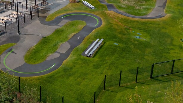 Een woonwijk met een kronkelende weg en een park met banken en een overdekte zitplek.
