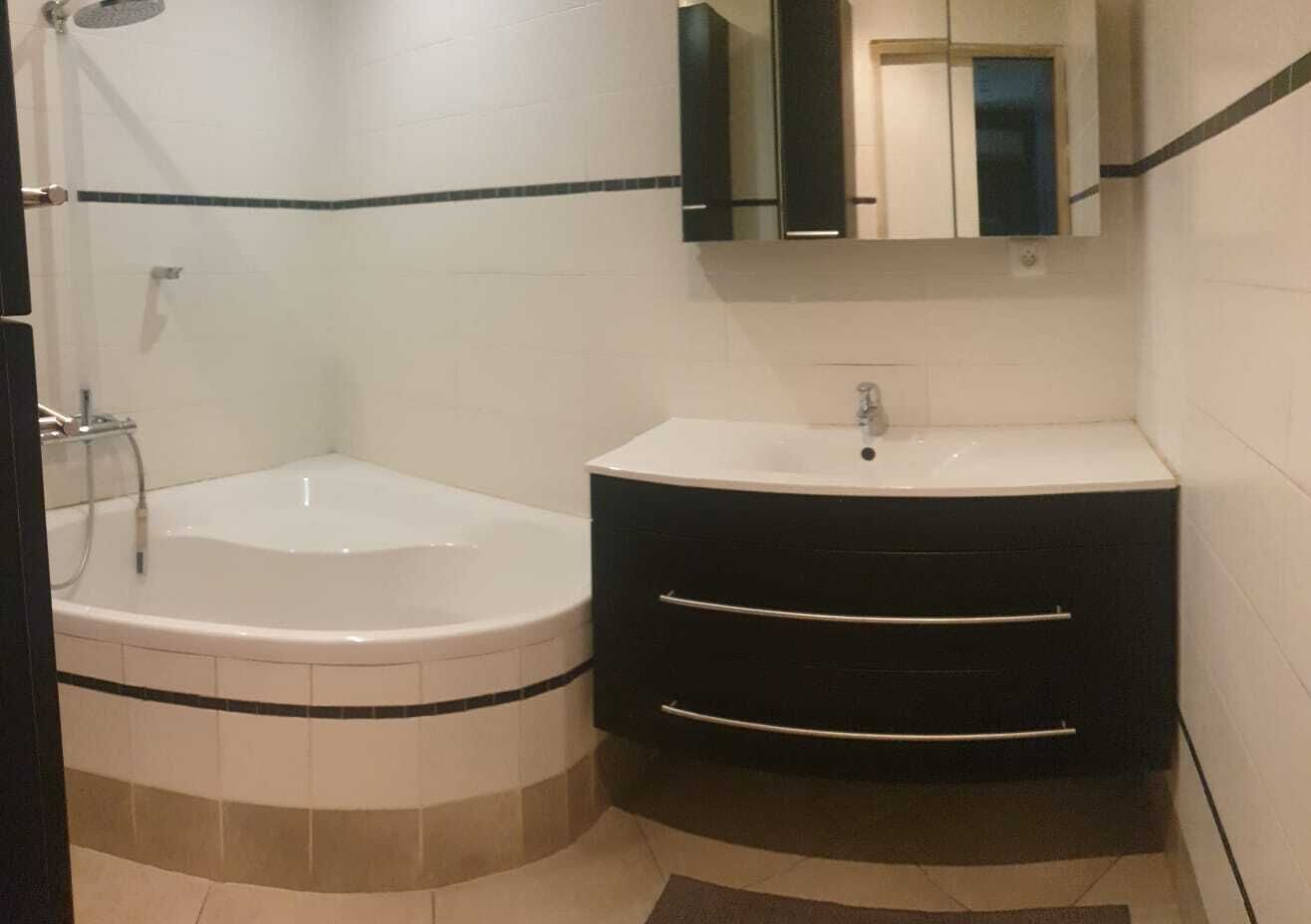 A bathroom with a corner bathtub, a white sink, and a black vanity with drawers.