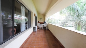 Un balcón con suelo de baldosas, una mesa y sillas, y vistas a palmeras.