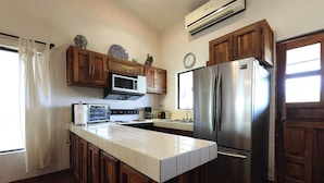 Una cocina con armarios de madera, un refrigerador de acero inoxidable, un microondas y una encimera azulejada.