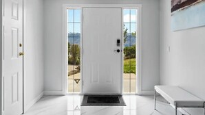 Un hall d’entrée propre et moderne, avec une porte blanche, un banc et une vue sur un paysage montagneux grâce à de grandes fenêtres.