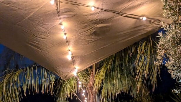 An outdoor seating area with chairs and a table, under a canopy with string lights. - Near Palermo Airport (PMO): Private Villa with Garden, Ideal for Families (Carini)