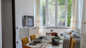 A dining area with a table set for four, a television on a stand, and a sofa in the background. - Near Palermo Airport (PMO): Private Villa with Garden, Ideal for Families (Carini)