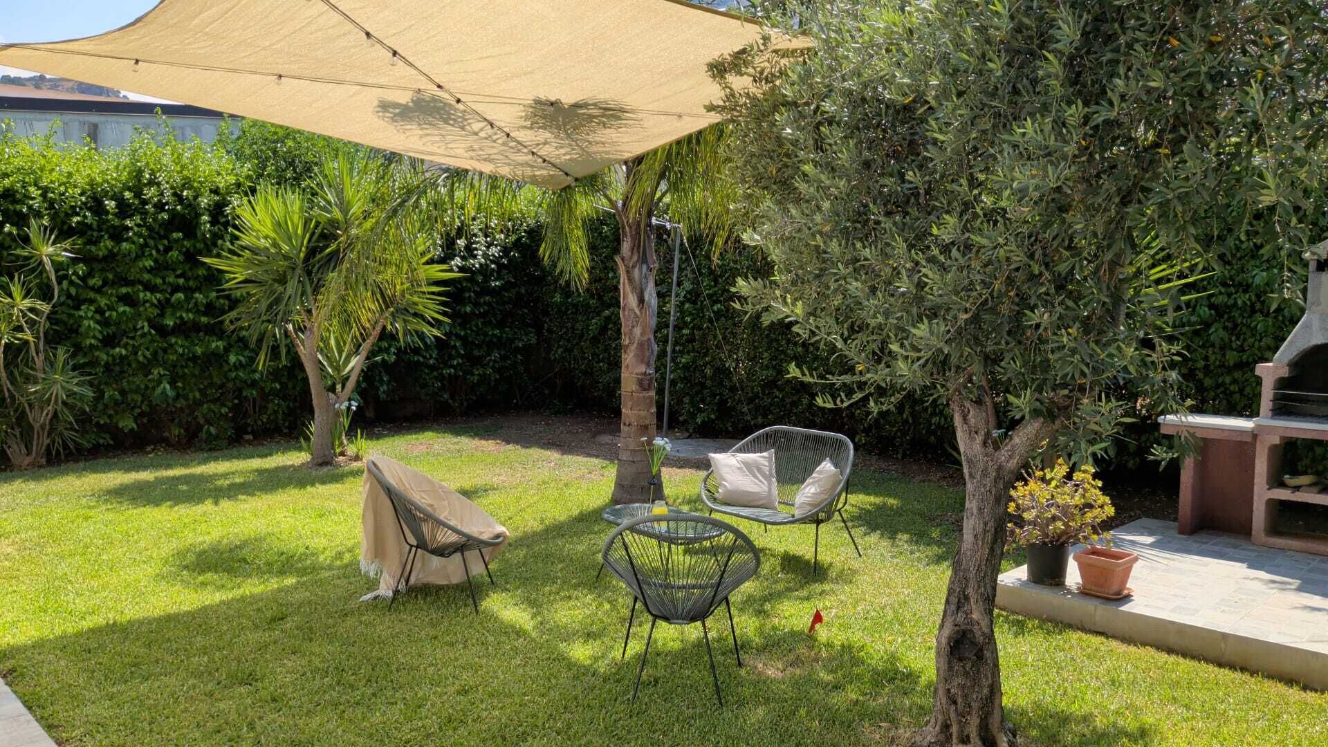 Ein gepflegter Garten mit Grillplatz, Gartenmöbeln und einer Pergola, die Schatten spendet.