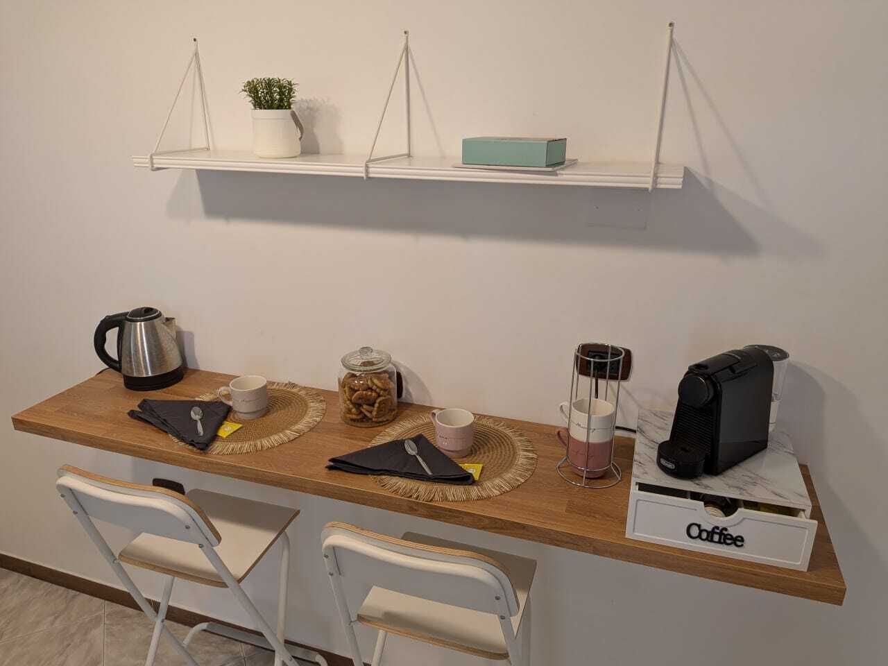 A kitchenette with a coffee maker, kettle, and jar of snacks on a wooden counter.