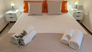 A neatly made bed with white bedding and orange pillows, two bedside lamps, and two rolled towels on a beige quilted bed runner. - Near Palermo Airport (PMO): Private Villa with Garden, Ideal for Families (Carini)