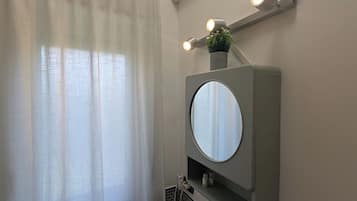 Een badkamer met een ronde spiegel, een kleine plant in een pot en een lamp boven de spiegel.