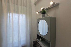Une salle de bain avec un miroir rond, une petite plante en pot et un luminaire placé au-dessus du miroir.