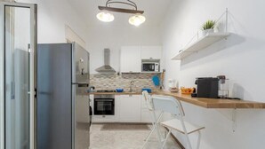 A compact kitchen with a refrigerator, microwave, stove, and a small sink. There are white cabinets, a wooden countertop, and a chair. - Near Palermo Airport (PMO): Private Villa with Garden, Ideal for Families (Carini)