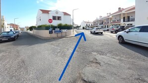 Une vue de rue avec un bâtiment blanc, des voitures garées et une flèche bleue sur la chaussée.