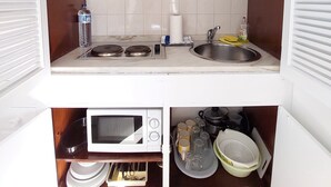 Une cuisine de taille réduite avec des meubles blancs, un four à micro-ondes, un évier et une cuisinière.