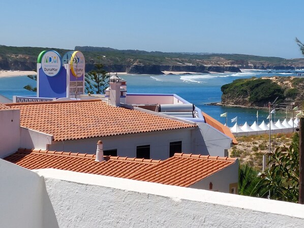 A coastal hotel with a red-tiled roof, white walls, and a view of the sea.