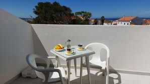 Un petit balcon extérieur avec une table dressée pour deux personnes, agrémenté d’un panier de fruits et d’une cafetière.