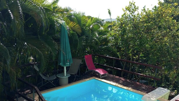 A rectangular swimming pool with a tiled border, surrounded by a wooden deck and a metal railing. - Atypical cottage ideally located for visiting the whole of Martinique.  (Rivière-Salée)