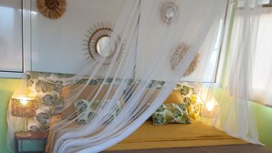 A bed with a canopy, a nightstand with a lamp, and decorative wall art. - Atypical cottage ideally located for visiting the whole of Martinique.  (Rivière-Salée)
