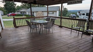 Überdachte Terrasse im Freien mit Tisch und Stühlen, einer Steinmauer und Blick auf eine Wohngegend mit Häusern und Wohnmobilen.