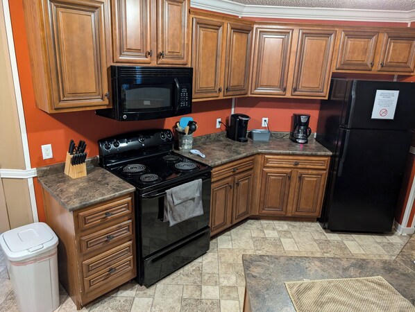 A kitchen with wooden cabinets, a black stove, a microwave, a refrigerator, and a coffee maker. - The Overlook at Robinson Point! (Mountain Home)