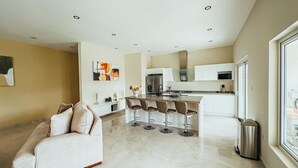 A modern kitchen with a central island, white cabinetry, and a stainless steel range hood. - Your second home in Aruba (Oranjestad)
