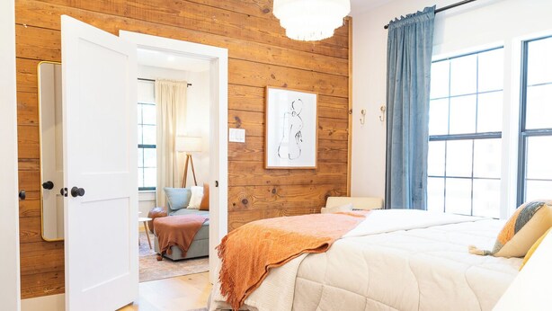A bedroom with a large bed, a wooden wall, a window with curtains, and a door leading to another room.
