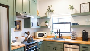 A kitchen with green cabinets, a microwave, a kettle, and a coffee maker.