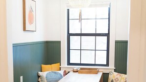 A cozy room with a wooden table, green upholstered bench seating, a window with a grid pattern, and a hanging light fixture.