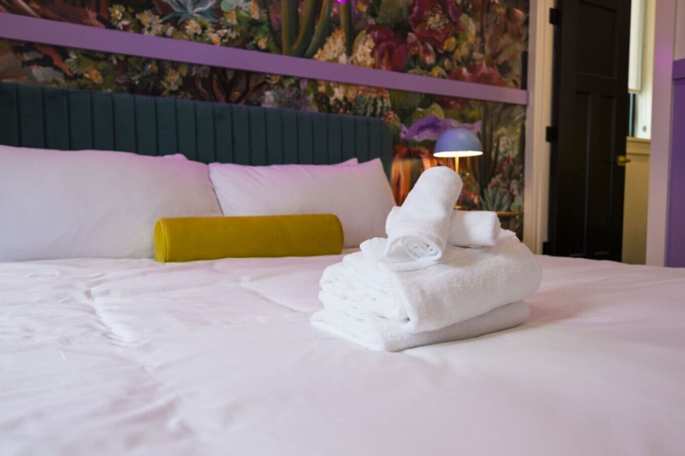 A neatly made bed with white linens and a stack of folded towels.