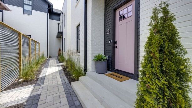 Une maison moderne avec une allée étroite, une porte rose et une petite plante en pot placée sur les marches.