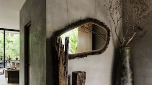 A modern interior with a concrete wall, a large mirror, and a rustic wooden sculpture. - Casa Kutzi Kutzi Paradise Villa Beach Club Access (Tulum)