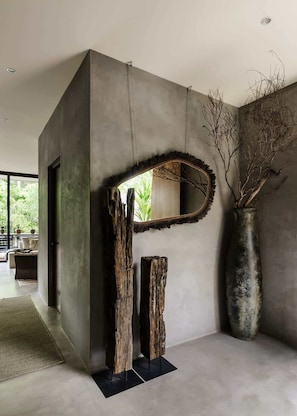 A modern interior with a concrete wall, a large mirror, and a rustic wooden sculpture. - Casa Kutzi Kutzi Paradise Villa Beach Club Access (Tulum)