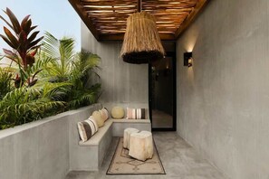 A modern outdoor seating area with a concrete bench, a woven ceiling light, and tropical plants.