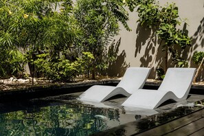 Relax by the serene pool surrounded by lush greenery and tranquil water reflections.