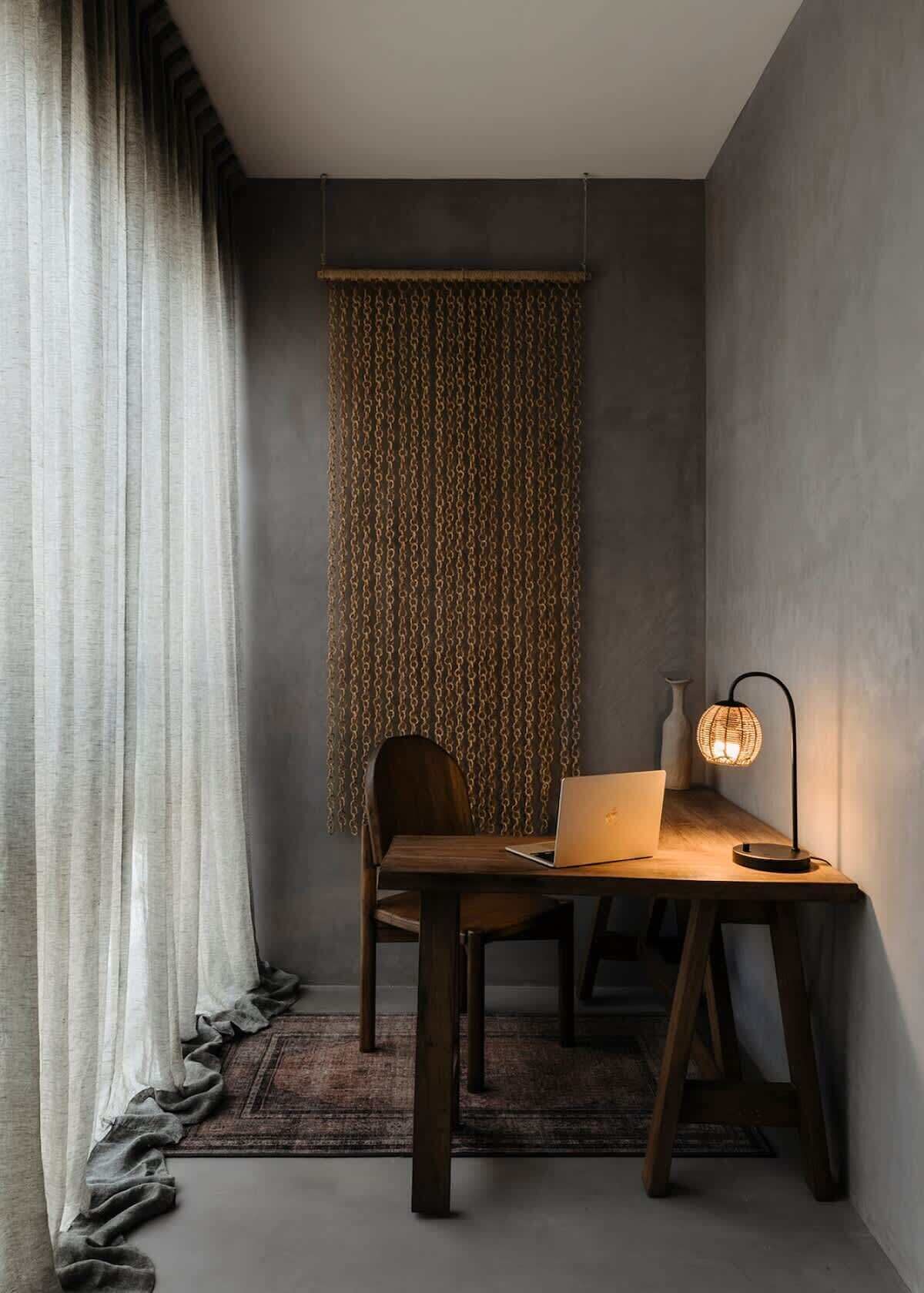 Een moderne kamer met een bureau, stoel, laptop en een lamp.
