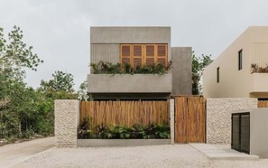 A modern two-story house with a concrete facade, a wooden fence, and a gravel driveway. - Casa Kutzi Kutzi Paradise Villa Beach Club Access (Tulum)