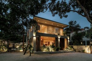 A modern two-story house with a large glass entrance, surrounded by trees and plants.