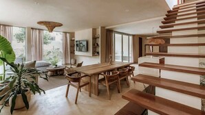 Un interior moderno con una mesa de comedor de madera, sillas, un sofá y una escalera.