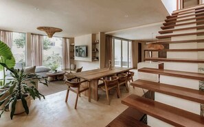 A modern interior with a wooden dining table, chairs, a sofa, and a staircase. - Casa Kunah Jungle Retreat Villa Beach Club Access (Tulum)