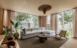 A modern living room with a sectional sofa, a round coffee table, and a wicker chair. - Casa Kunah Jungle Retreat Villa Beach Club Access (Tulum)