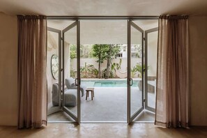 A room with a sliding glass door leading to an outdoor pool area, a sofa, and a small table. - Casa Kunah Jungle Retreat Villa Beach Club Access (Tulum)