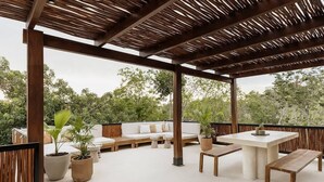 Un patio al aire libre con una pérgola de madera, un conjunto de sofás, una mesa y plantas en macetas.