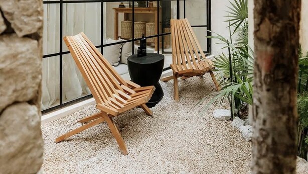 Een modern interieur met een glazen wand, houten stoelen, een geweven hangstoel en kamerplanten.