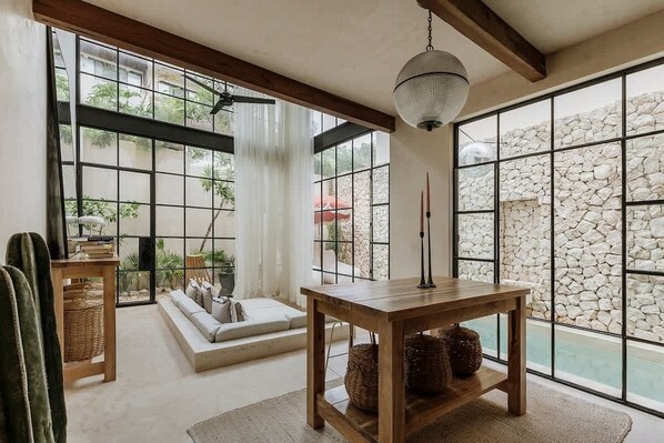 A room with a large window, a wooden table, a sofa, and a stone wall.