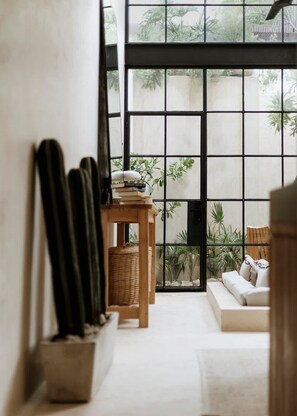 A room with a large window, a wooden table with books and a plant, a sofa, and a cactus in a pot.