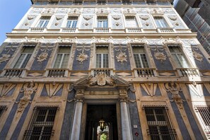Un edificio imponente de arquitectura clásica, con elaboradas esculturas, ventanas amplias y una entrada destacada con un toldo decorativo.