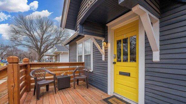 A wooden deck with two chairs and a bench, a yellow door, and a mailbox. - Game Room + Fenced Yard - King Bed - Pet Friendly (Wichita)