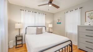 A bedroom with a bed, bedside lamps, a ceiling fan, a dresser, and a framed picture on the wall. - Game Room + Fenced Yard - King Bed - Pet Friendly (Wichita)