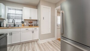 A modern kitchen with white cabinets, a stainless steel refrigerator, and a wooden countertop. - Game Room + Fenced Yard - King Bed - Pet Friendly (Wichita)