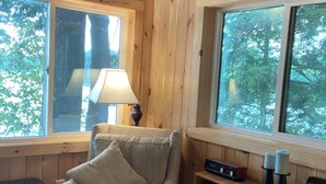 Una habitación acogedora con paredes de madera, un sillón mullido, una lámpara y una estantería con diversos objetos.