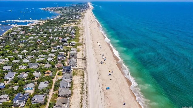 Vista aérea de una zona residencial costera con casas a lo largo de la playa, aguas azules cristalinas y barcos a lo lejos.