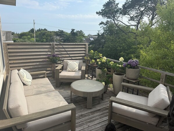 Una terraza de madera con mobiliario exterior, incluyendo un sofá, sillas y una mesa.