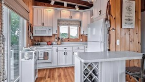 Una cocina con armarios blancos, microondas, refrigerador y un botellero.